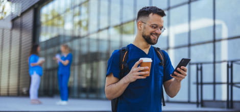 Doctor checking his phone outside a hospital holding a coffee